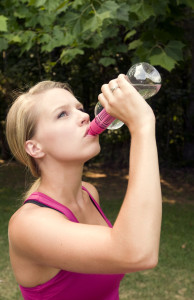 A young woman drinks water while exercising. 