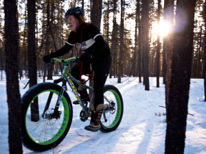 A woman winter cycling in the woods with over sized tires.